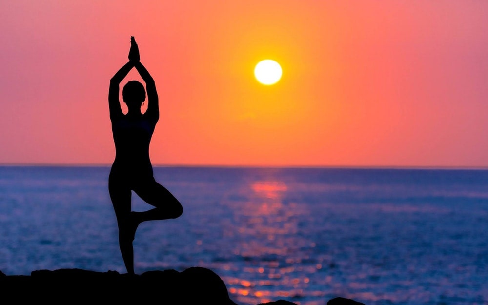 Silhouette of woman practicing yoga at the beach during sunset
